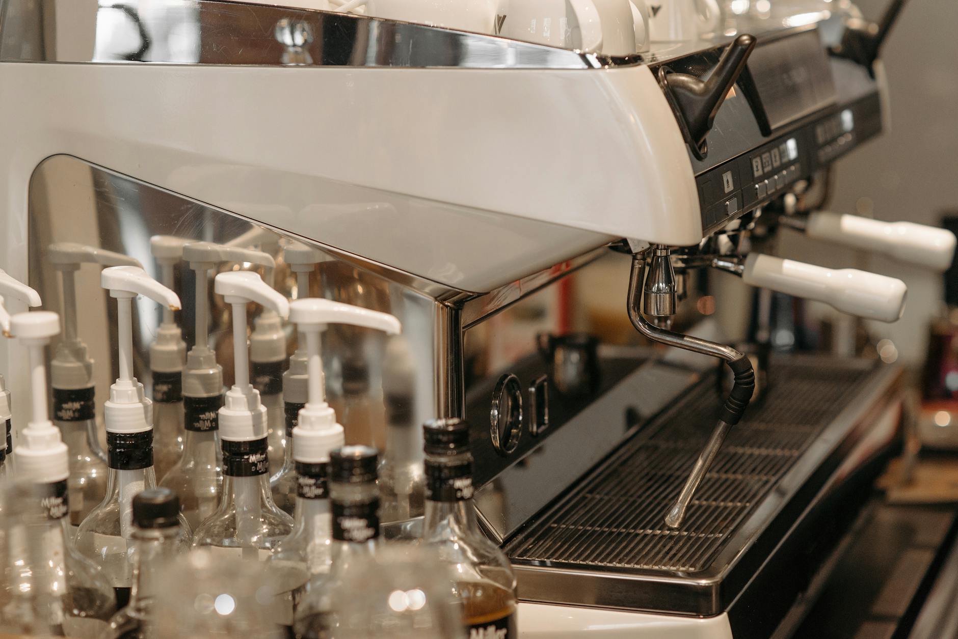 A close-up view of a professional espresso machine with syrup bottles in a coffee shop setting.